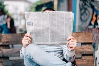 persona su una panchina con un quotidiano aperto davanti al viso